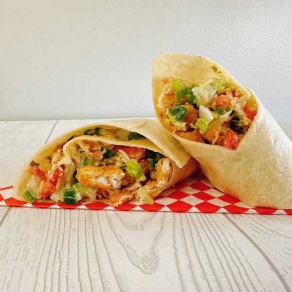 Two crispy chicken wraps filled with lettuce, tomatoes, and green onions on a red checkered paper.