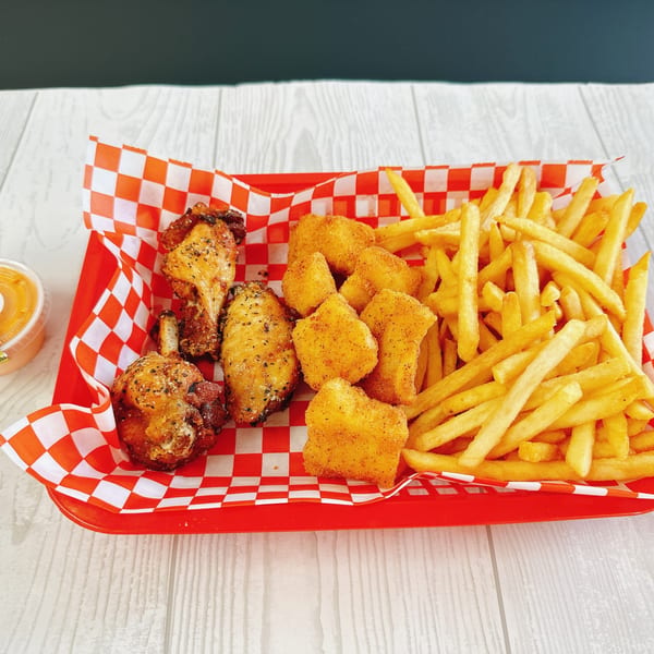 A red basket with checkered paper holds fried chicken wings, golden nuggets, and crispy french fries.